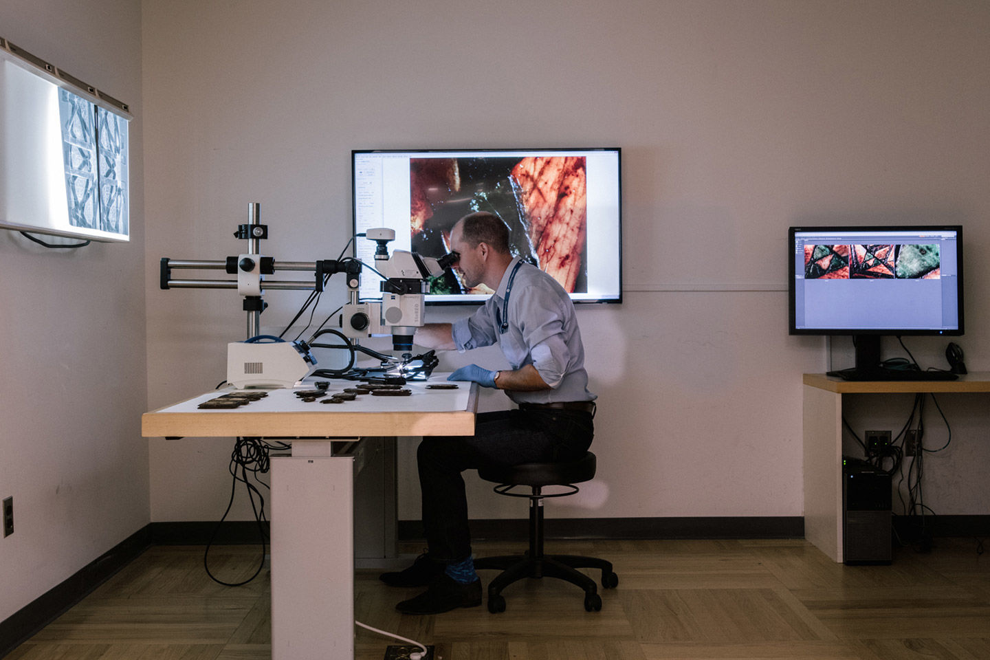 Man looking through a microscope surrounded by screens